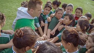 a male coach and a number of young girls in a sports huddle